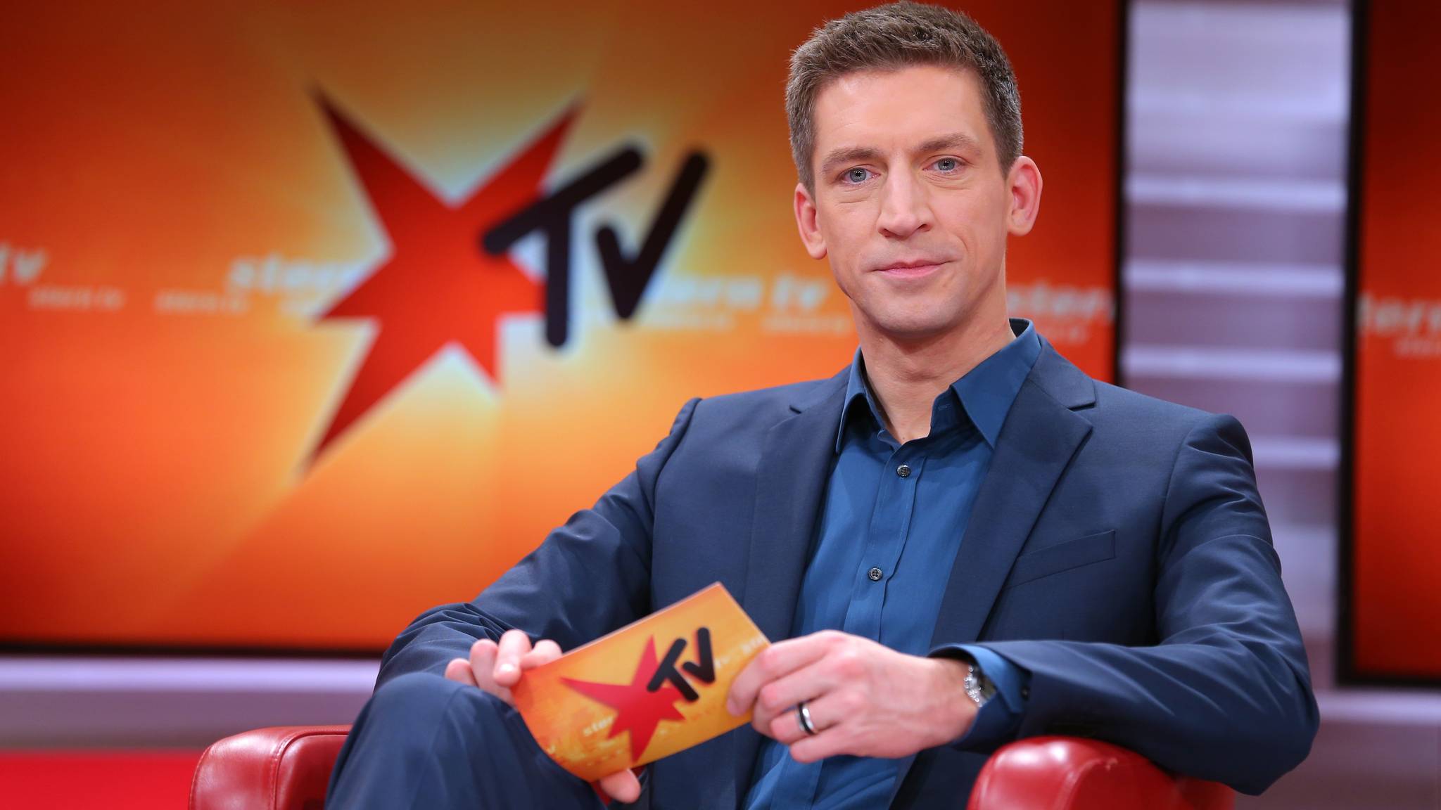 Steffen Hallaschka sitzt in einem eleganten grauen Anzug und blauem Hemd im Studio von stern TV auf einem roten Sessel und blickt in die Kamera.